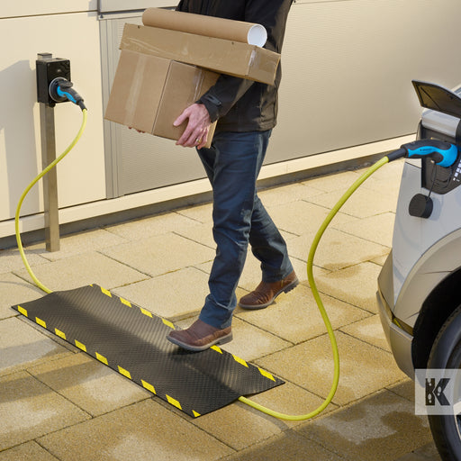 Kleen-Cable Mat EV - Man walks by an electric vehicle on charge while carrying a box. The mat prevents the trip hazard