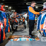 Ad-Mat - A person standing on a custom printed advertisement mat with a motorcycle in the background and biker jackets.