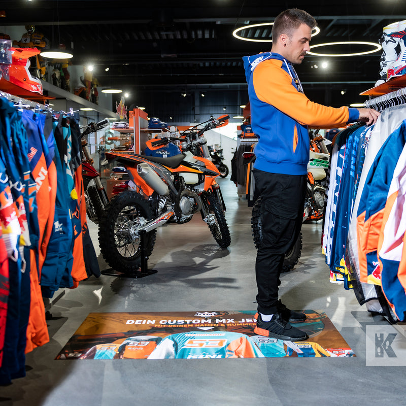 Ad-Mat - A person standing on a custom printed advertisement mat with a motorcycle in the background and biker jackets.