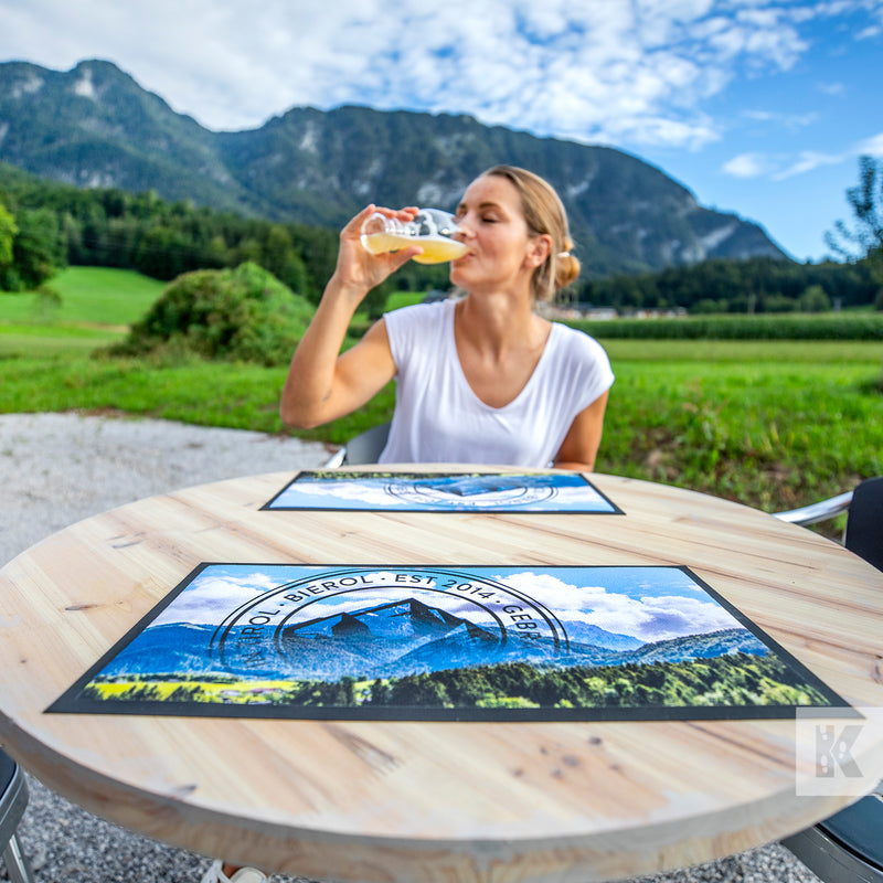 Bar-Mat - Lady enjoying a drink of beer in an outdoor nature setting with printed mats on a solid wood table top