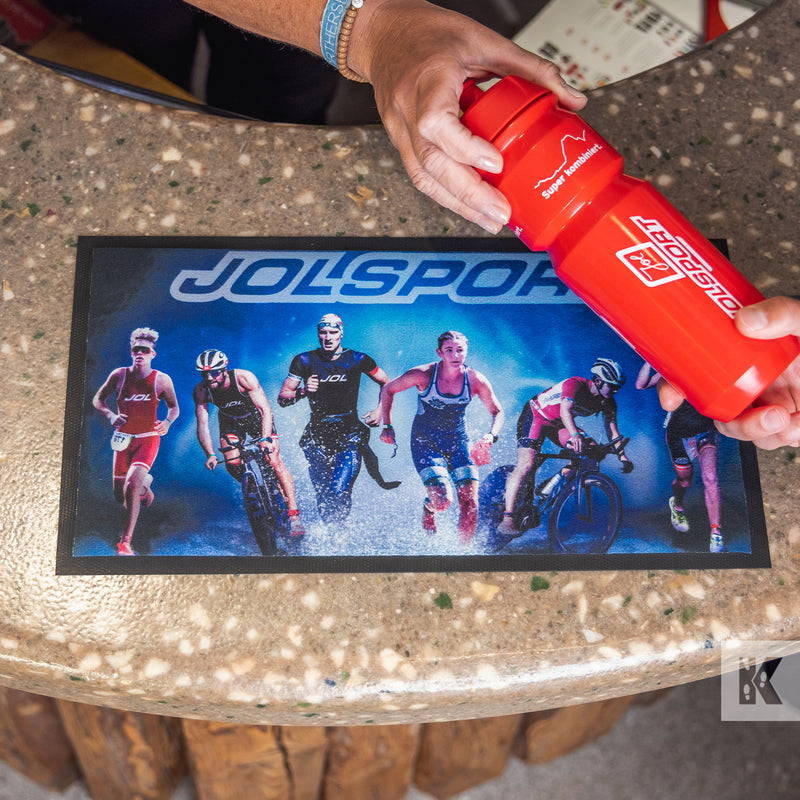 Counter Mat - Jolsport branded mat on a counter with a branded water-bottle handed to the teller