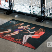 Ad-Mat - Four attractive ladies depicted on an Ad-Mat in the Riedel factory store, positioned in front of a display of glasses.