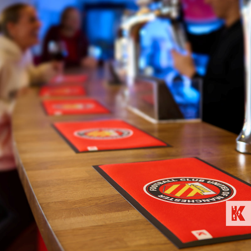 Bar-Mat - FC United of Manchester mats on a bar top with people having fun in the background