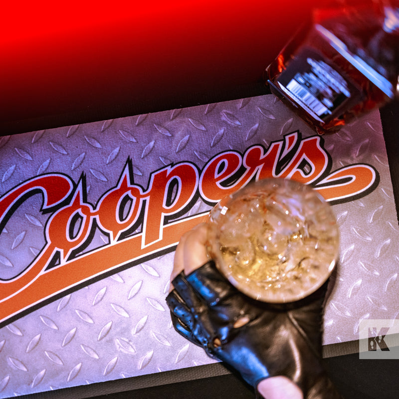 Bar-Mat - Coopers graphics with a metal effect background printed on a Bar Mat, a hand in a fingerless glove holds a drink