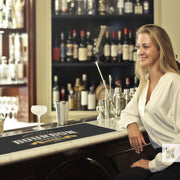 Bar-Mat - Sophisticated lady in a bar scene waiting to be served, lots of beverages in bottles and a mat printed with a Bourbon slogan