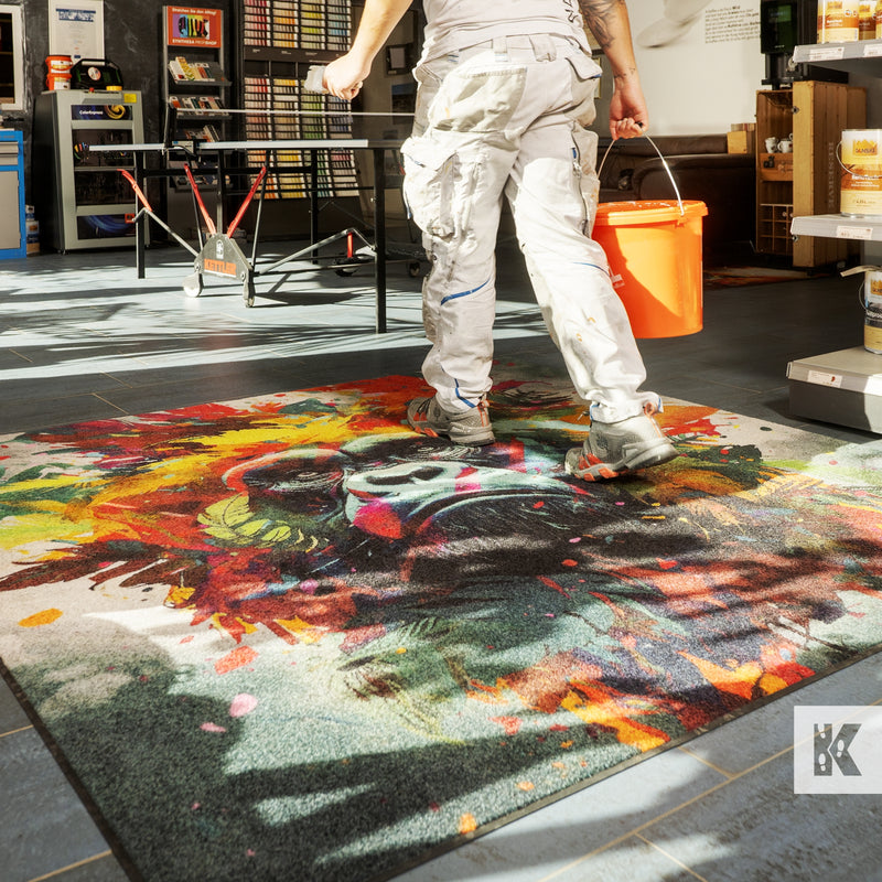 Jet-Print Light - Detailed and colourful artistic image of a chimpanzee on a printed mat, a man in white clothes carries an orange bucket across