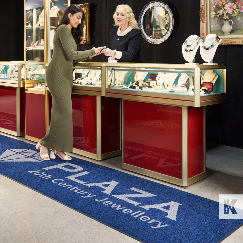 Jet-Print Light - Plaza Jewellery blue logo mat in front of a display where a young lady is considering a purchase