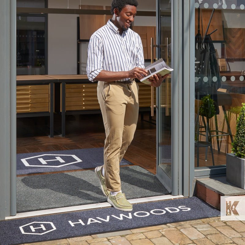 Jet-Print Outdoor - Man walking out of a store with a pamphlet, crossing a Havwoods branded outdoor mat