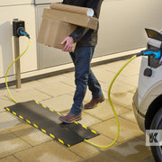 Kleen-Cable Mat EV - Man walks by an electric vehicle on charge while carrying a box. The mat prevents the trip hazard