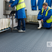 Modular grey floor matting with drainage holes, two men are preparing for work in overalls with a sink and many wellies