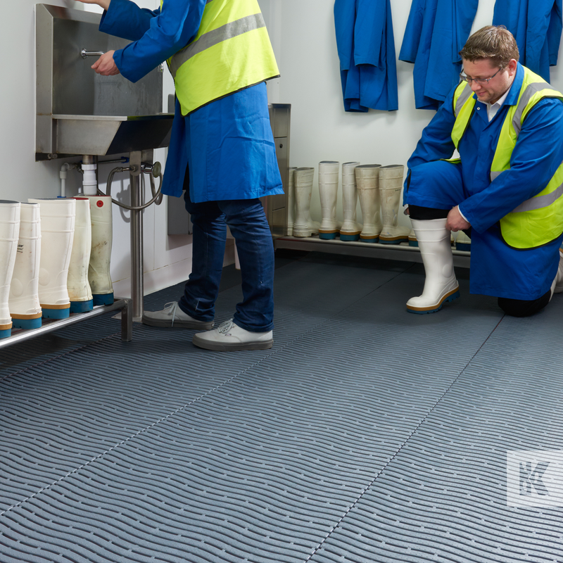 Modular grey floor matting with drainage holes, two men are preparing for work in overalls with a sink and many wellies