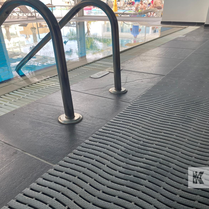 Textured black drainage matting on a pool deck with pool area in the background