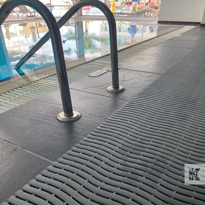 Textured black drainage matting on a pool deck with pool area in the background