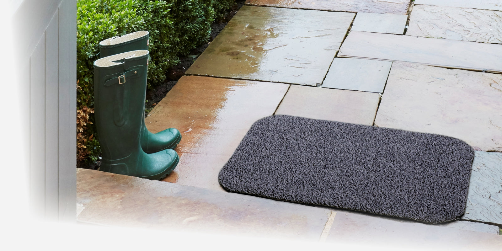 Outdoor weather proof scraper mat with green wellies on a stone path