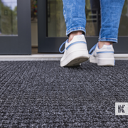 Water-Horse - Close up of a mat positioned at an outside entrance with a person entering the building