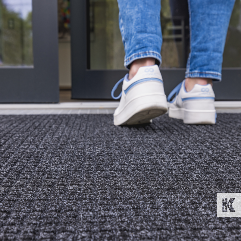 Water-Horse - Close up of a mat positioned at an outside entrance with a person entering the building