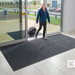 Man with a suitcase exiting a building onto a doormat