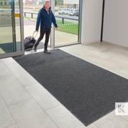 Man with a suitcase exiting a building onto a long textured mat.