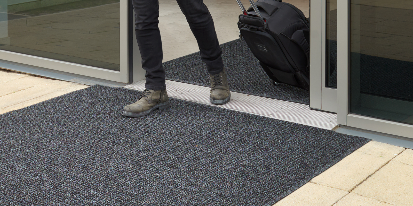 Person stepping onto a textured black mat from a glass door entrance.
